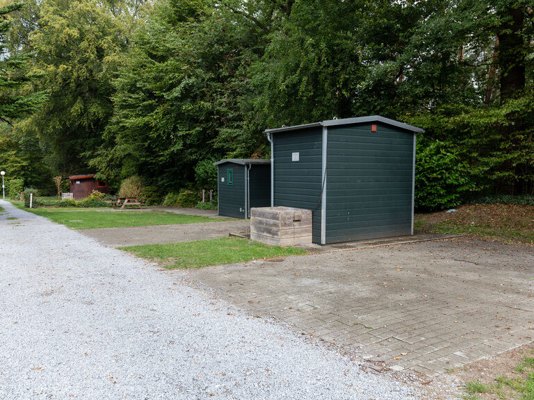 Ein grüner Schuppen steht am Rand eines Feldwegs im Freien.