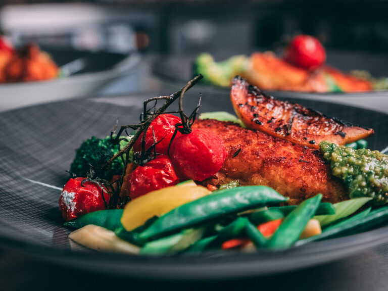 Ein Teller mit saftigem Hühnchen und frischem Gemüse auf einem minimalistischen Tischgedeck.